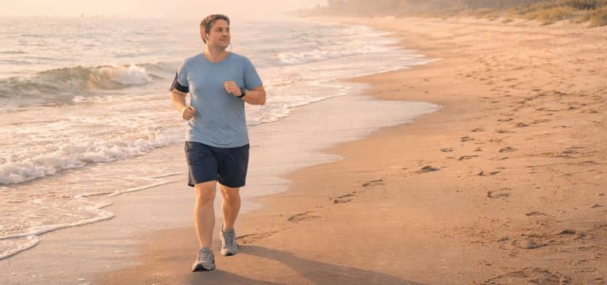 A middle-aged man, a beginner runner, jogging slowly along the beach in the early morning, with soft sunlight, a relaxed posture, casual running attire, and a peaceful, natural atmosphere.