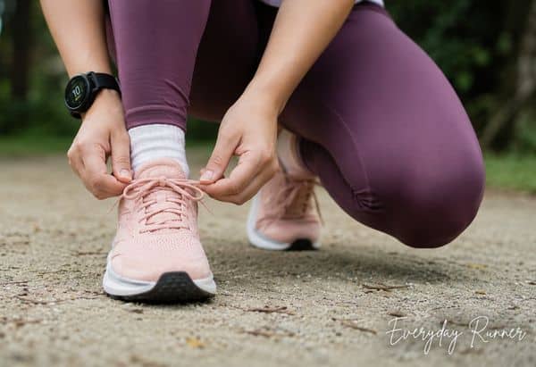 Everyday Runner preparing for a run by tying running shoe laces outdoors, wearing purple leggings, white socks