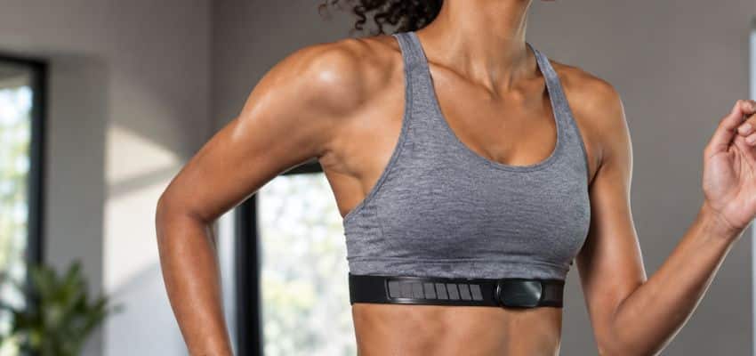 Runner in a gray sports bra wearing a running watch and chest heart-rate sensor to compare readings when checking for cadence lock.